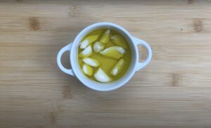 White bowl with garlic cloves in olive oil on wooden background. Perfect for cooking and flavoring dishes.